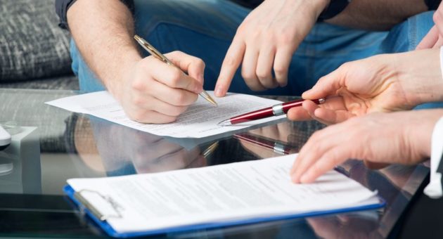 Two people reviewing and signing documents on a glass table