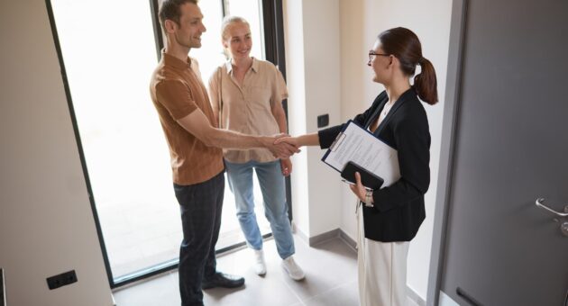 high angle picture of a young woman holding a clipboard poised as a real estate agent shaking hands with a young couple