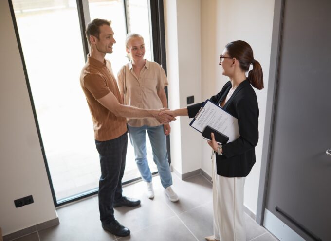 high angle picture of a young woman holding a clipboard poised as a real estate agent shaking hands with a young couple