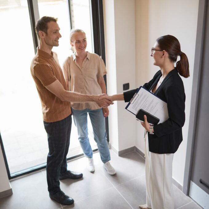 high angle picture of a young woman holding a clipboard poised as a real estate agent shaking hands with a young couple