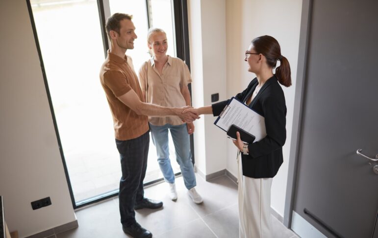 high angle picture of a young woman holding a clipboard poised as a real estate agent shaking hands with a young couple