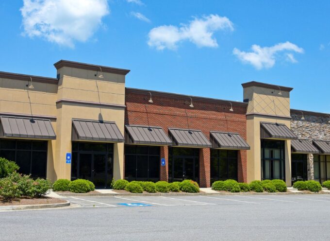 Empty multi-unit commercial retail building with stone, brick, and stucco exterior under a clear blue sky