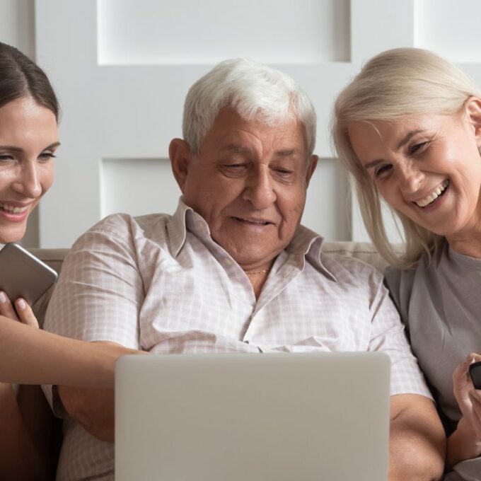 three people sitting on a couch looking at a computer while laughing and smiling and pointing to it