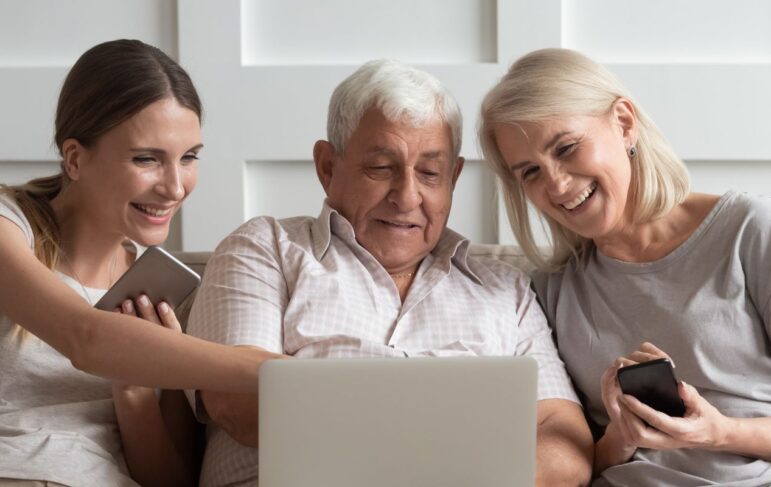 three people sitting on a couch looking at a computer while laughing and smiling and pointing to it